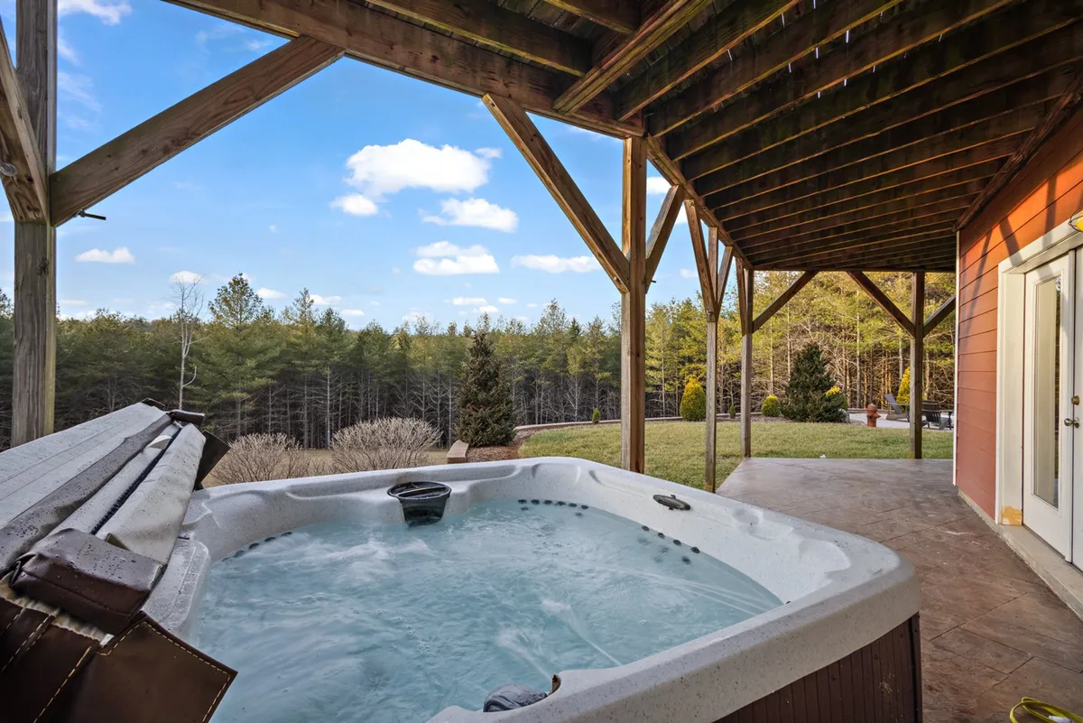 A bubbling hot tub is set against a backdrop of wooden beams and lush greenery, with open sky overhead. The area is tranquil and private, perfect for soaking in the natural surroundings.
