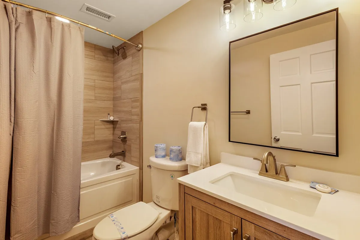 A serene, well-lit bathroom featuring a bathtub, sink, mirror, and toilet. The space feels fresh and inviting, with subtle touches for comfort and relaxation, ideal for unwinding after outdoor activities.