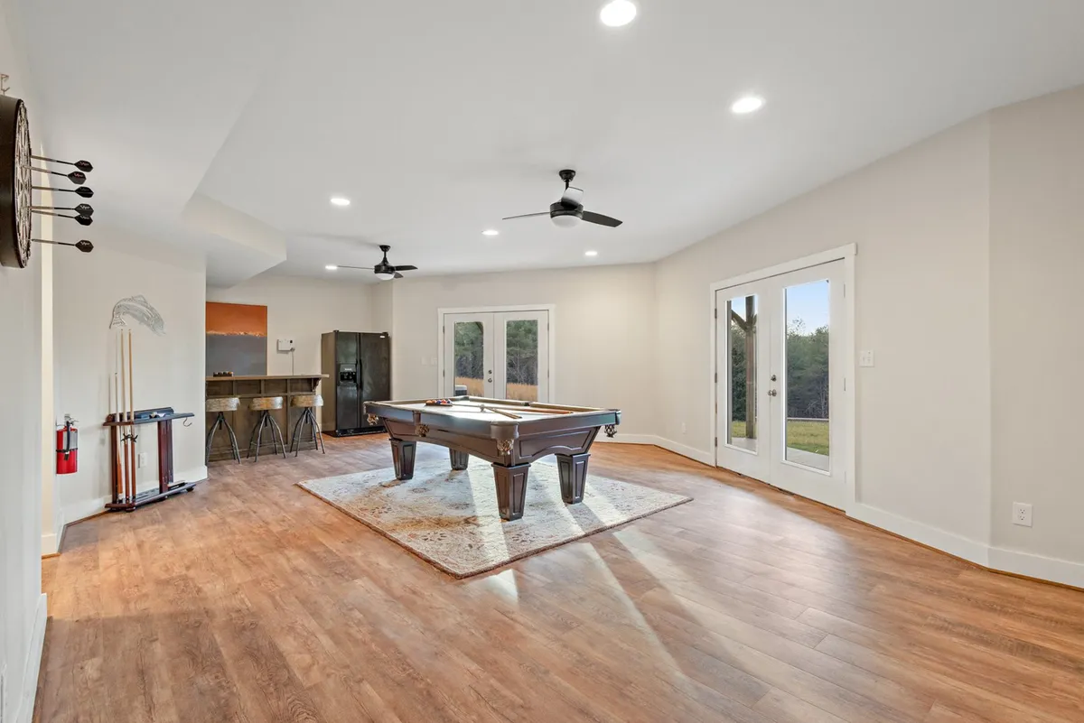 A spacious entertainment area featuring a pool table as the focal point, with plenty of natural light streaming in through the windows. The scene also showcases a wet bar area in the background, inviting guests to enjoy refreshments while participating in games or socializing.