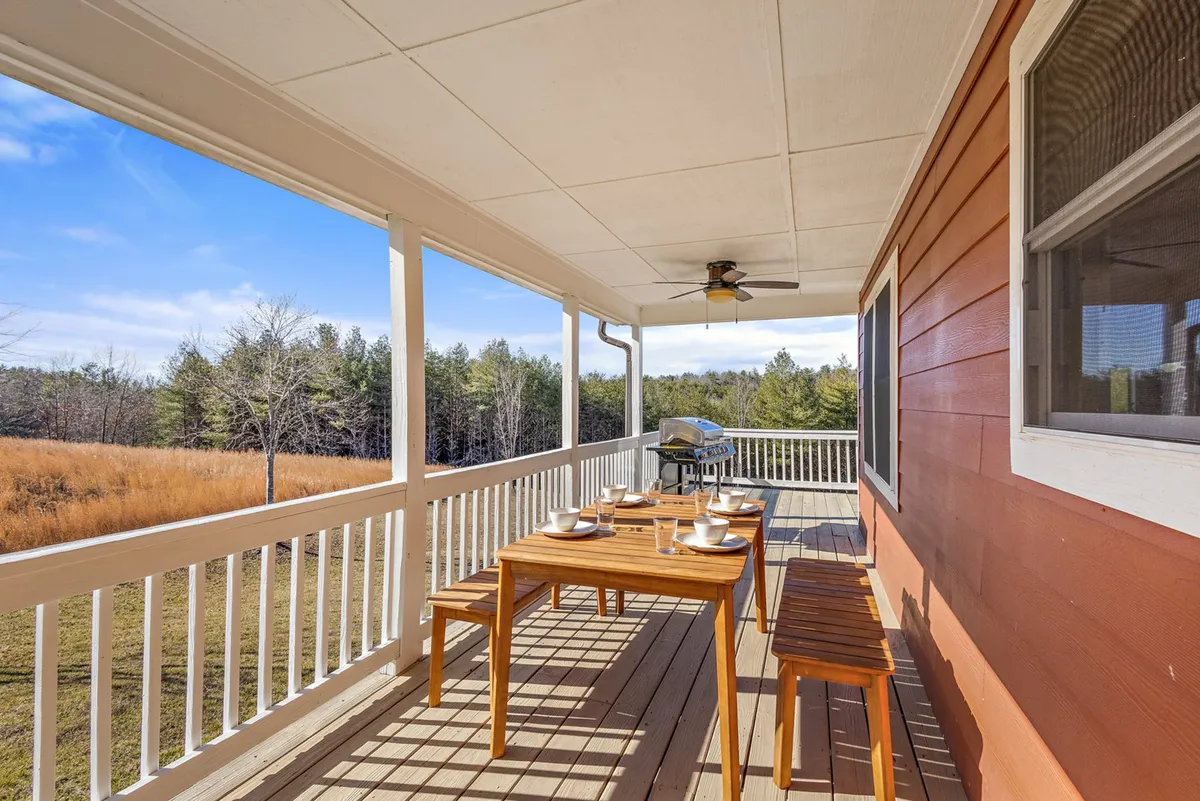This image features a wooden deck set up for outdoor dining, with a table arranged for tea and a grill nearby. The deck is surrounded by a sturdy railing and overlooks lush greenery, inviting guests to enjoy meals under the open sky.