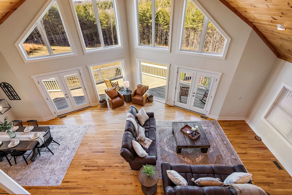 A spacious living room with comfortable seating positioned to take in the expansive forest views through large windows. The room’s design is warm and inviting, with natural wood details and a cozy atmosphere that invites relaxation or lively gatherings.