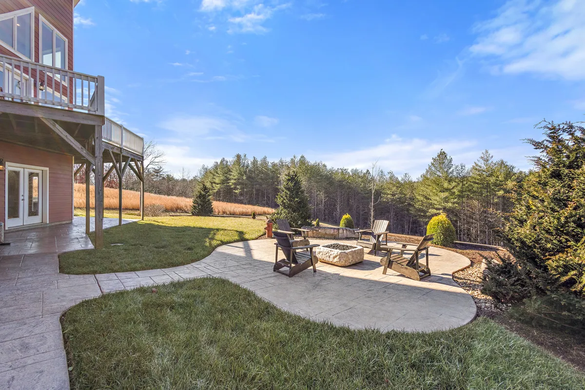 This exterior shot highlights a cozy fire pit area, surrounded by classic Adirondack chairs with a landscaped backdrop of trees and natural stone patio. The setting is ideal for outdoor gatherings, storytelling, and stargazing.