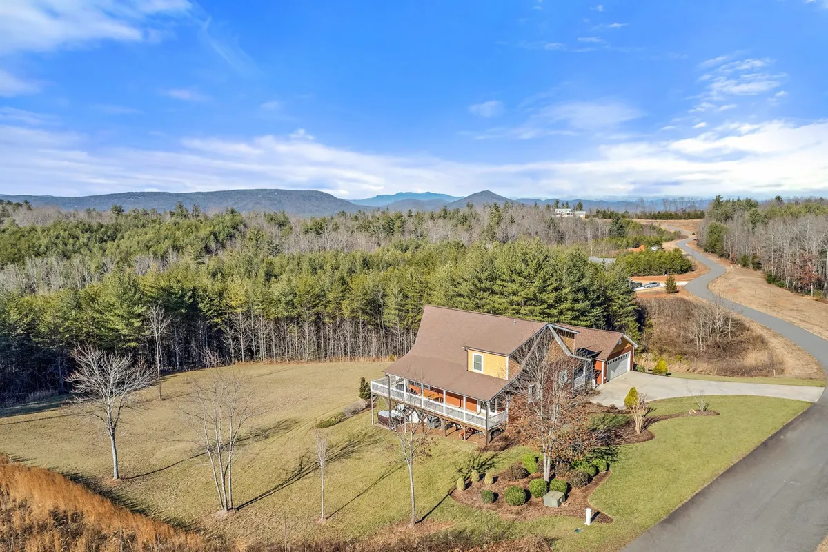 An expansive yard stretches out in front of a large house, bordered by mature trees and an open, grassy lawn. The space feels open and inviting, perfect for children's play and pets to romp freely.