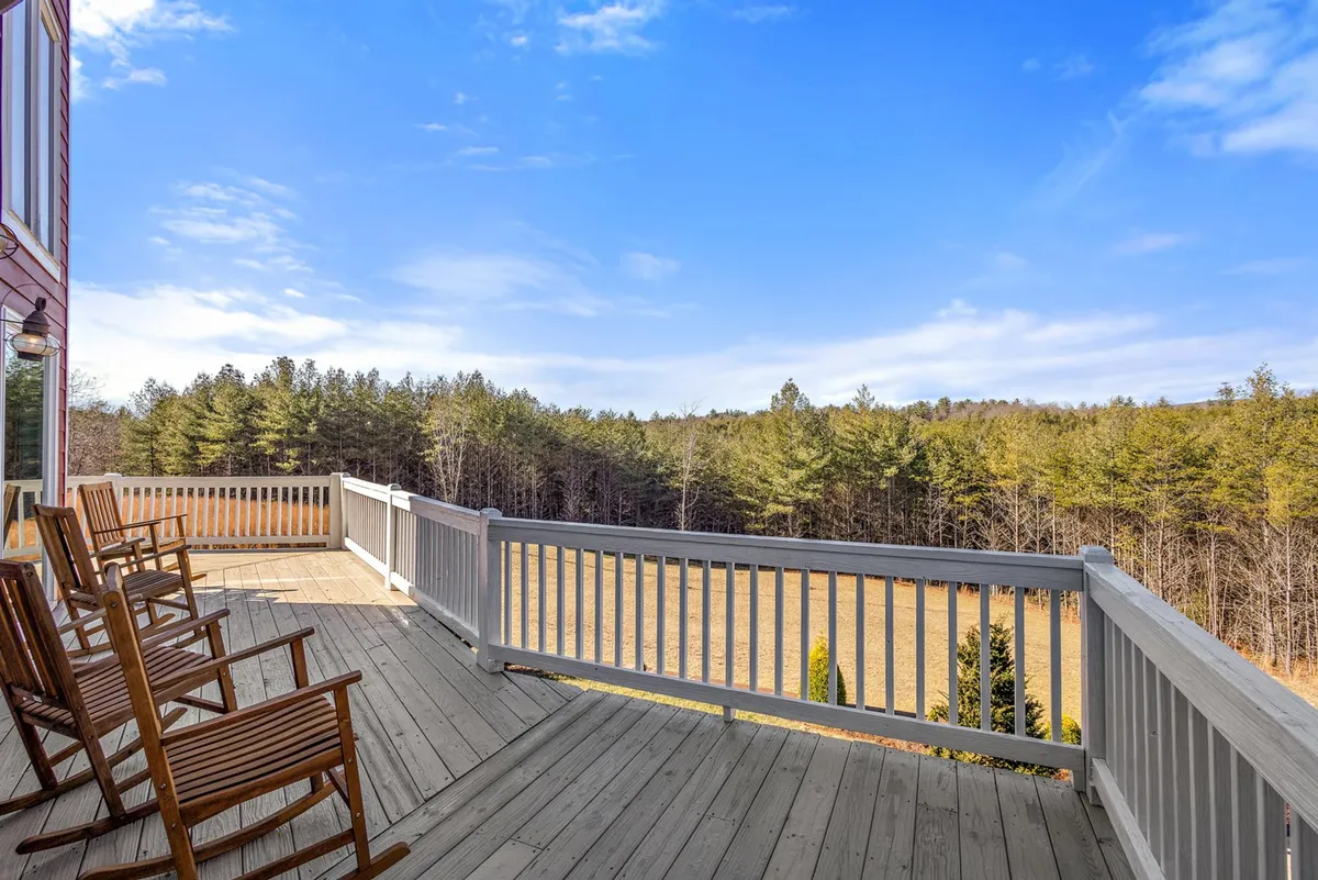 Featuring wooden rocking chairs on an expansive deck, this image offers a serene vantage point overlooking lush green trees. The setting encourages relaxation while immersing guests in nature, seamlessly blending the comfort of home with immediate access to forested surroundings and adventure.