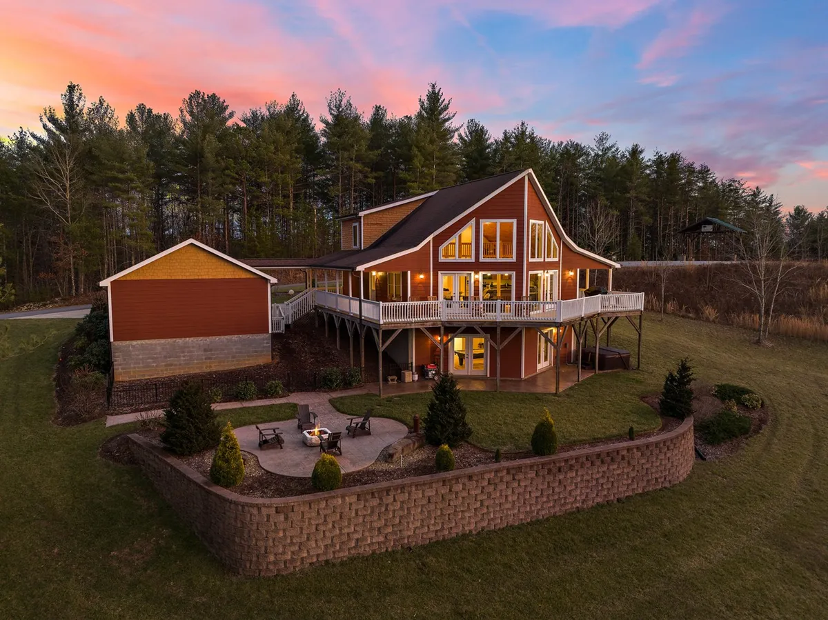 The image showcases House Galini’s striking modern exterior nestled in the woods, with a spacious deck overlooking sunset views. The deck flows into a cozy fire pit area, perfect for outdoor gatherings, evening fires, and family game nights under the stars. The atmosphere is warm and inviting, making the outdoor spaces a central feature of the experience.