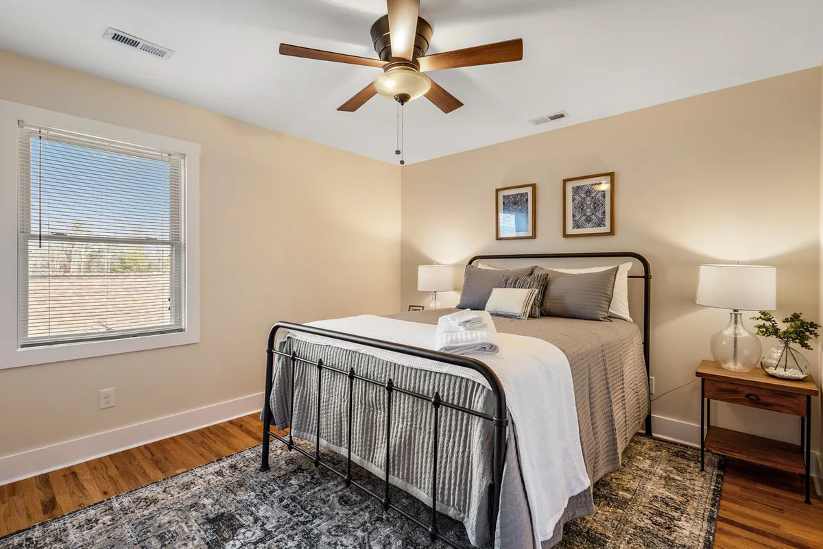 A master suite with a king bed adorned with decorative pillows, a nightstand with a lamp, and tasteful wall art. The room exudes calm and comfort, suggesting easy access to an outdoor deck through a nearby (not pictured) doorway.