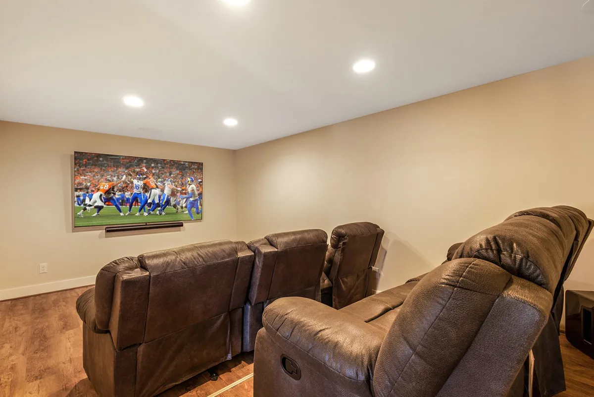 A cozy theater room with plush reclining chairs arranged in front of a large wall-mounted television, providing an ideal spot for immersive movie nights or game viewing. The mood is inviting and perfect for relaxation.