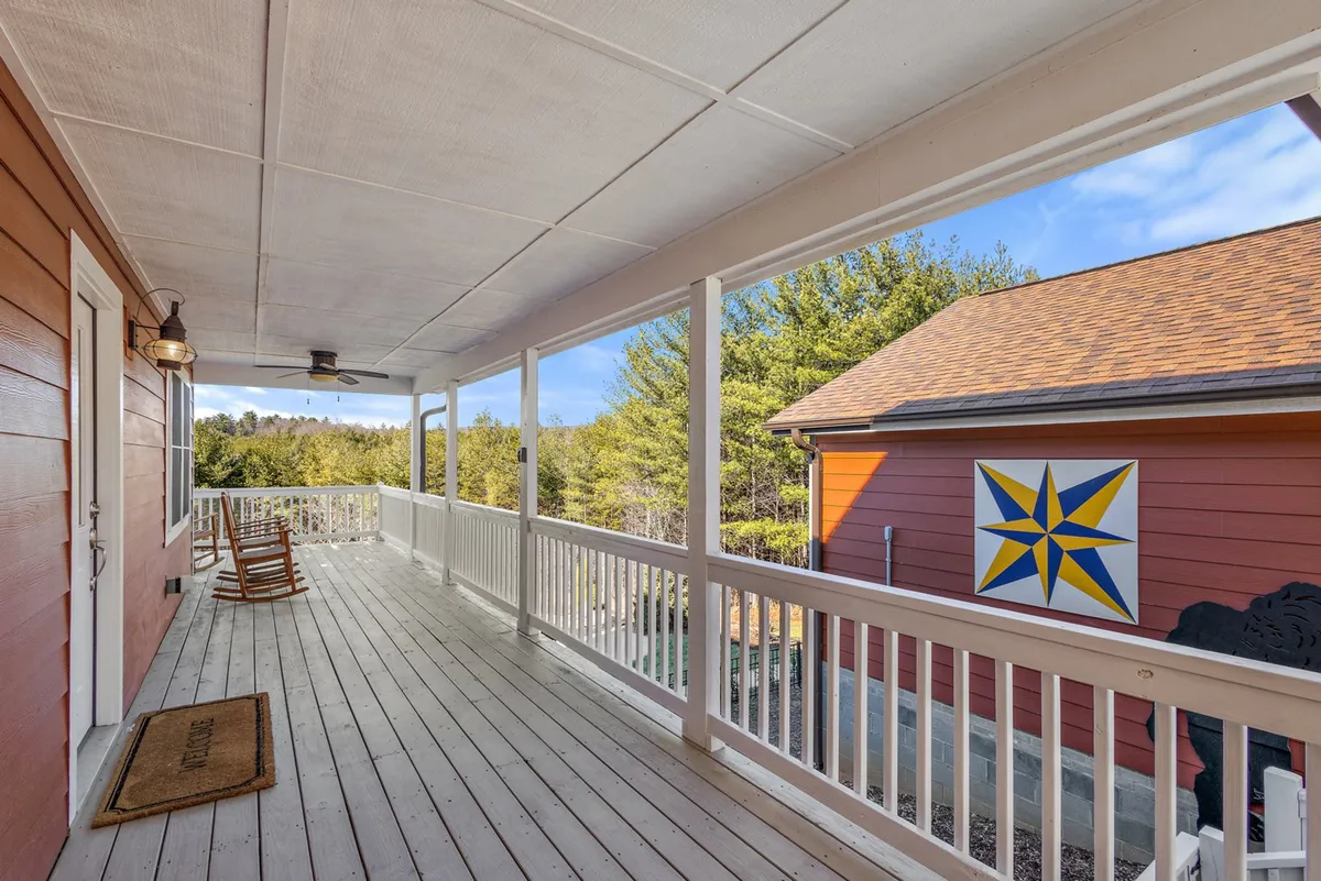 This inviting view highlights a cozy rocking chair and colorful star decoration on the porch, framed by a wooden railing and views of the treetops. The image captures a sense of relaxation and anticipation, with the outdoors and adventure beckoning just beyond the porch.