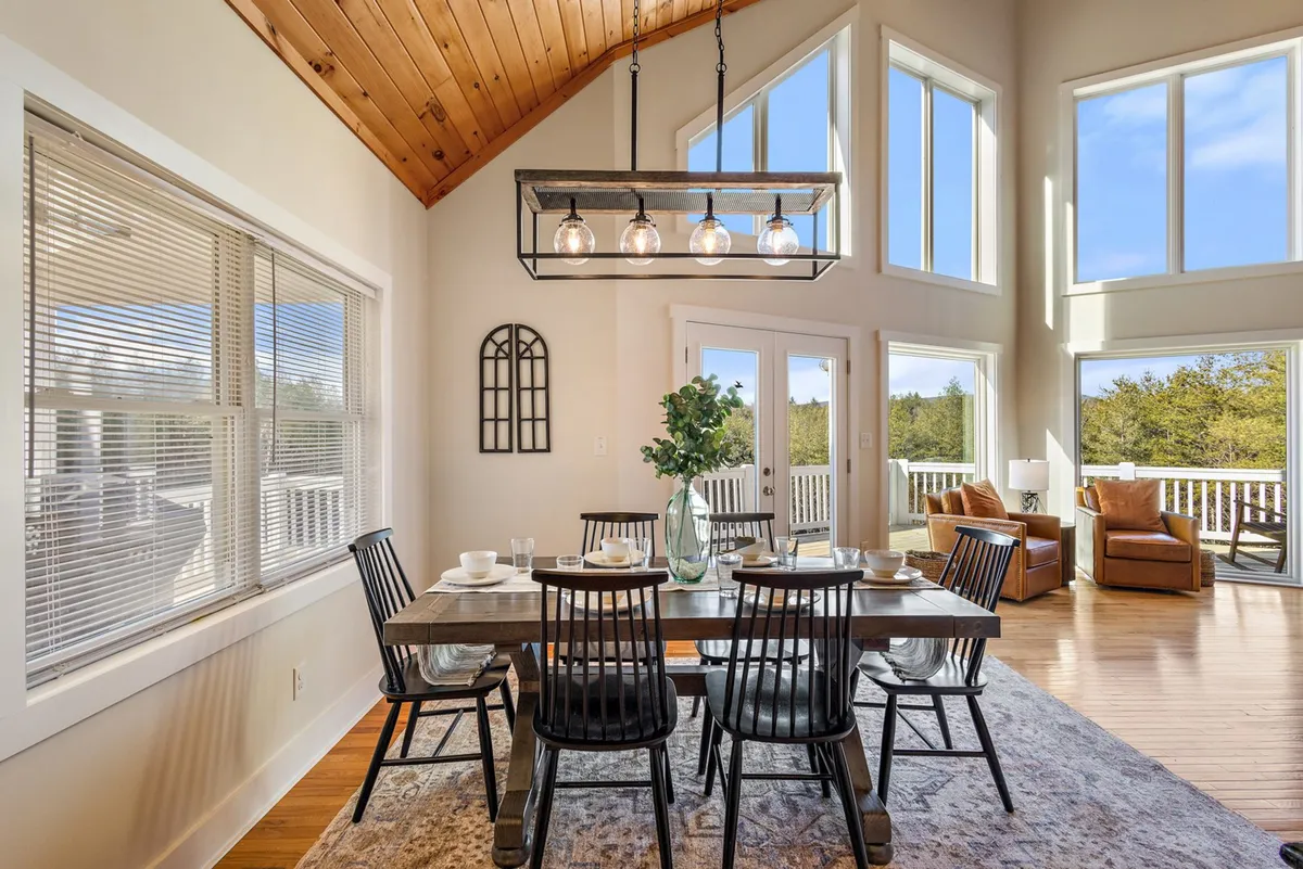 A spacious dining area with a large table, comfortable chairs, and a statement chandelier, all illuminated by generous natural light from expansive windows. The setup is ideal for shared meals, conversation, and enjoying sunset views, capturing the spirit of togetherness.