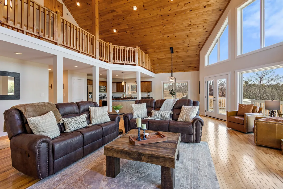 A bright, cozy living area with large windows framing views of the outdoors, comfortable seating, and a charming wooden ceiling. The space feels open and connected to the outside, suggesting an easy transition from outdoor adventures to indoor relaxation.